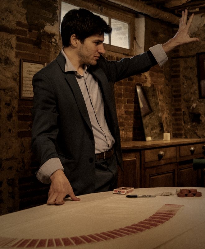 Jeremy Sulzer à une table de jeu, une main posée sur le tapis à côté d'un éventail de cartes, face à une spectatrice.