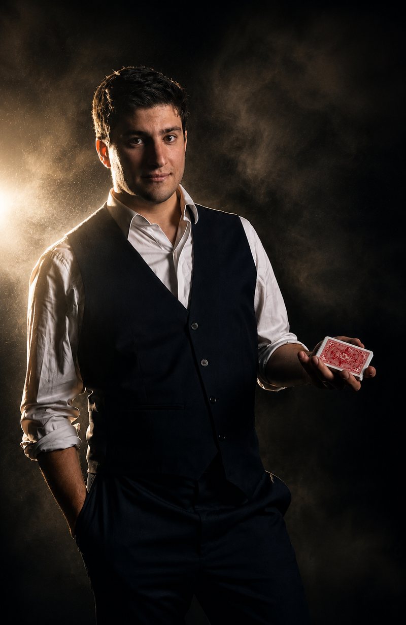 Portrait of Jeremy Sulzer in a dark waistcoat and white shirt, holding a deck of cards.